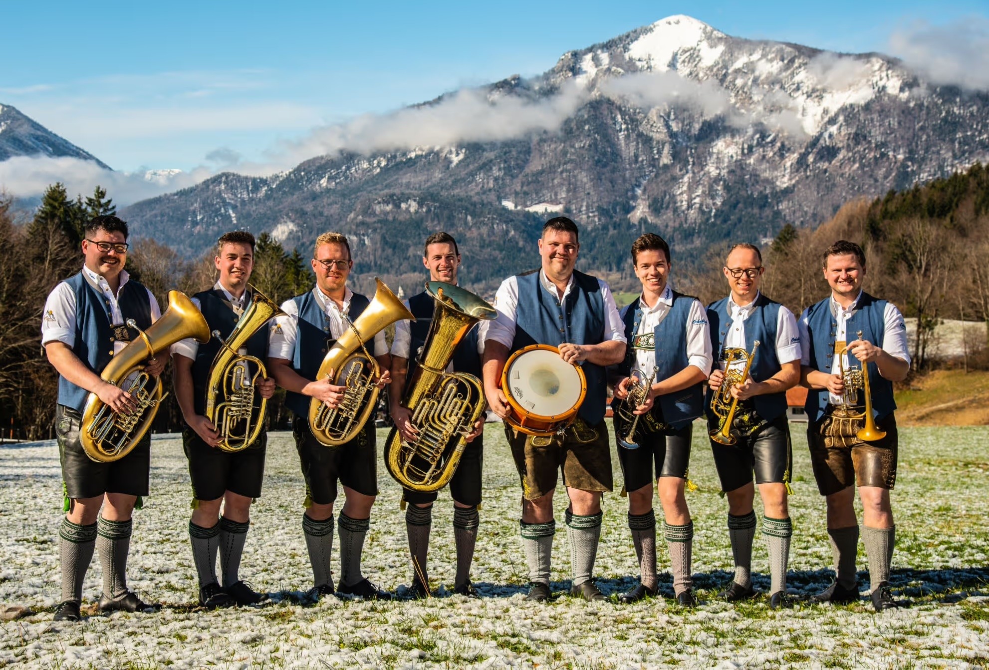 Die Musikgruppe Ochablech steht im Freien mit einem Berg im Hintergrund mit ihren Blasmusik Instrumenten in der Hand für ein Gruppenfoto