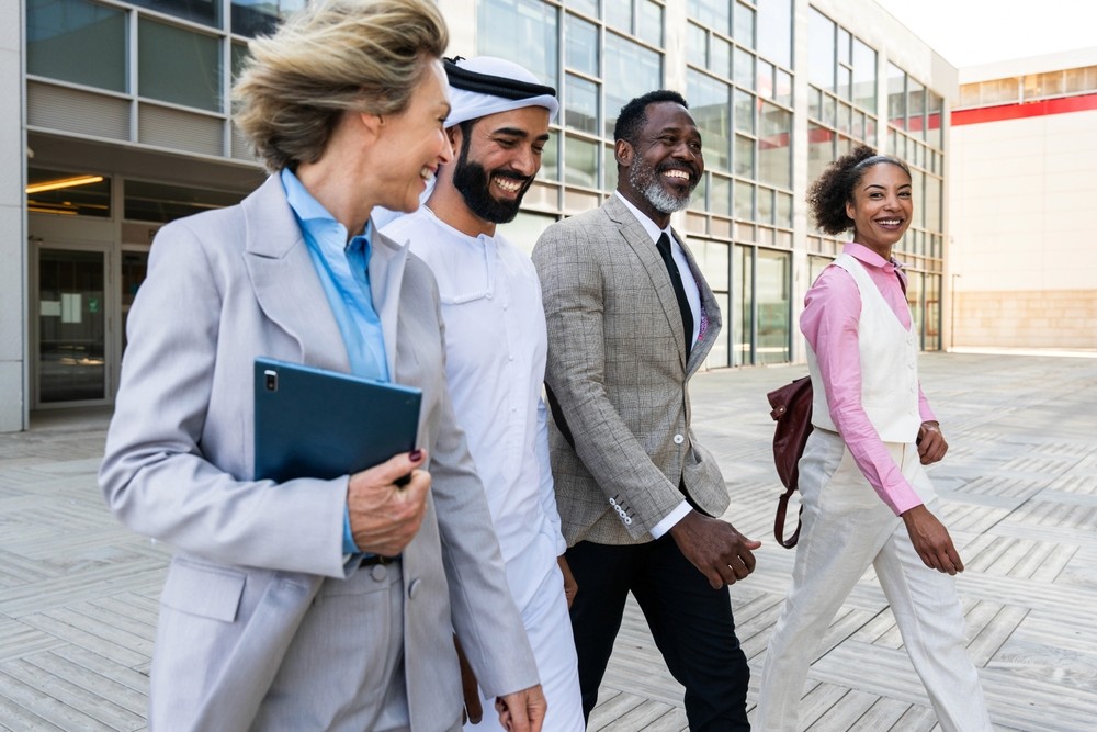 A diverse group of professionals walks outside a modern office building within the Ajman Free Zone business district.  