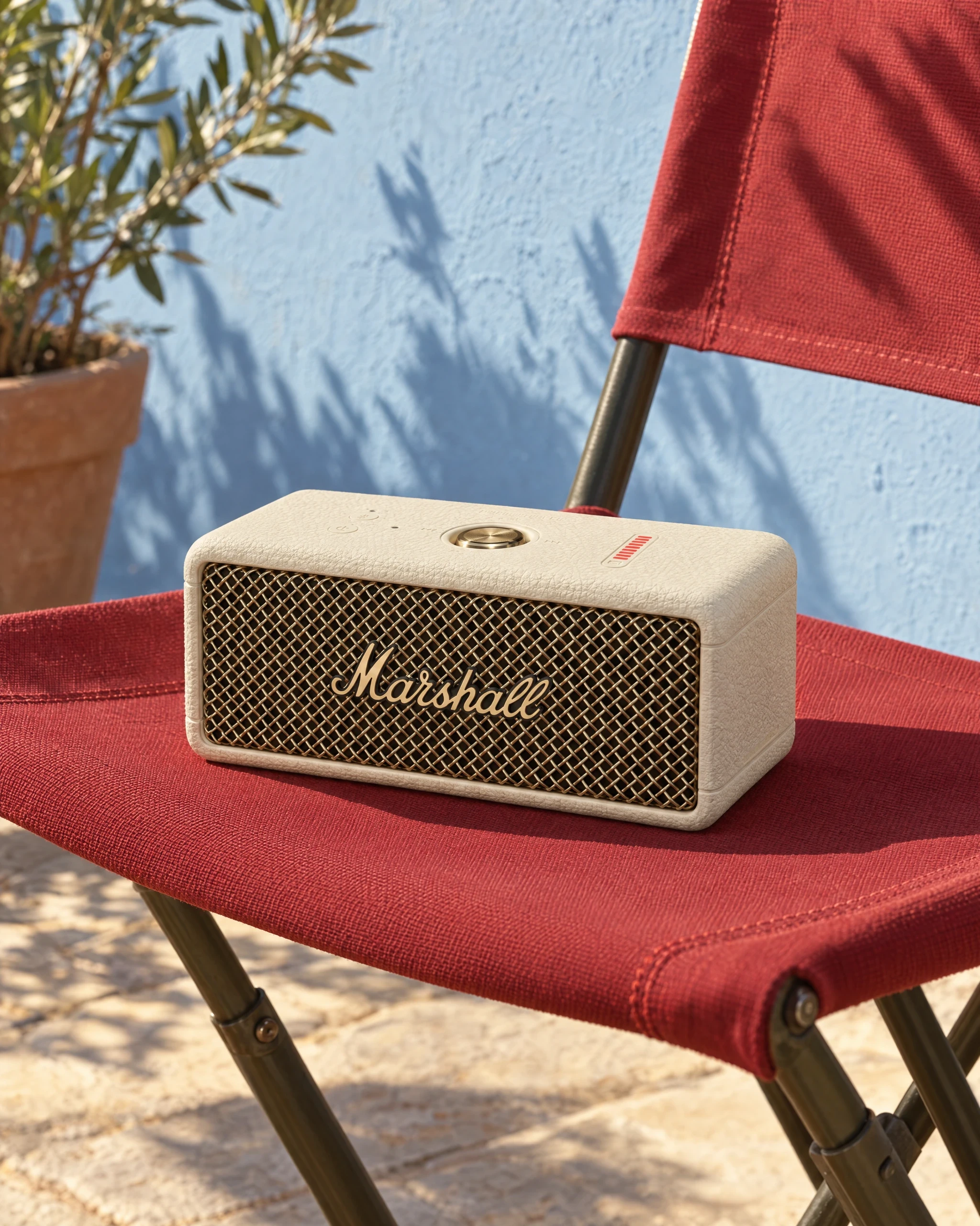 Cream Marshall Emberton III speaker on a red canvas chair against a blue wall