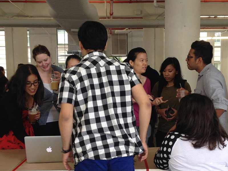 A photo of a group of people sitting near a stand and looking at a laptop.