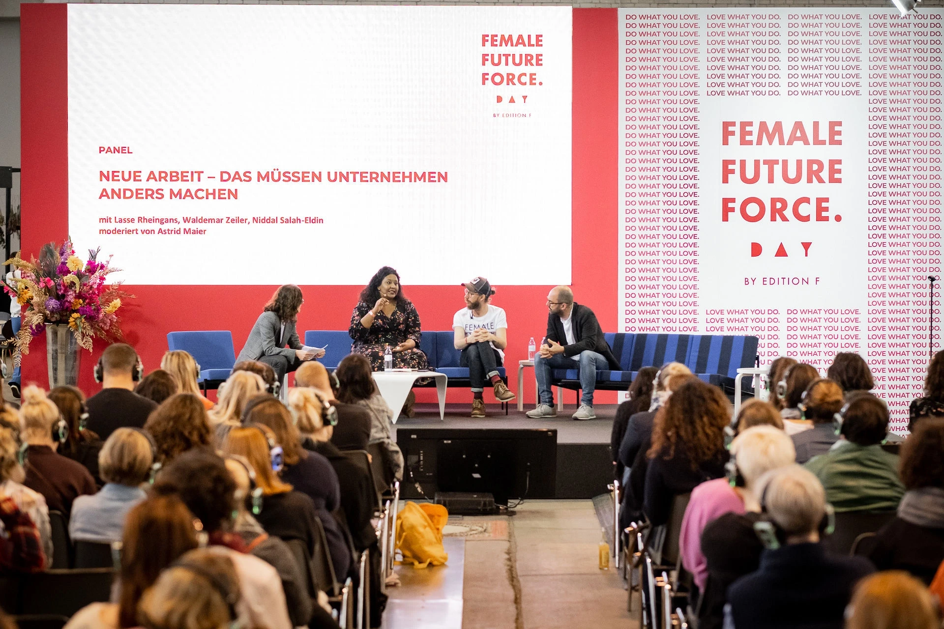 Panel discussion on new work on a red-and-white stage at Female Future Force Day, with speakers on blue sofas before the audience.
