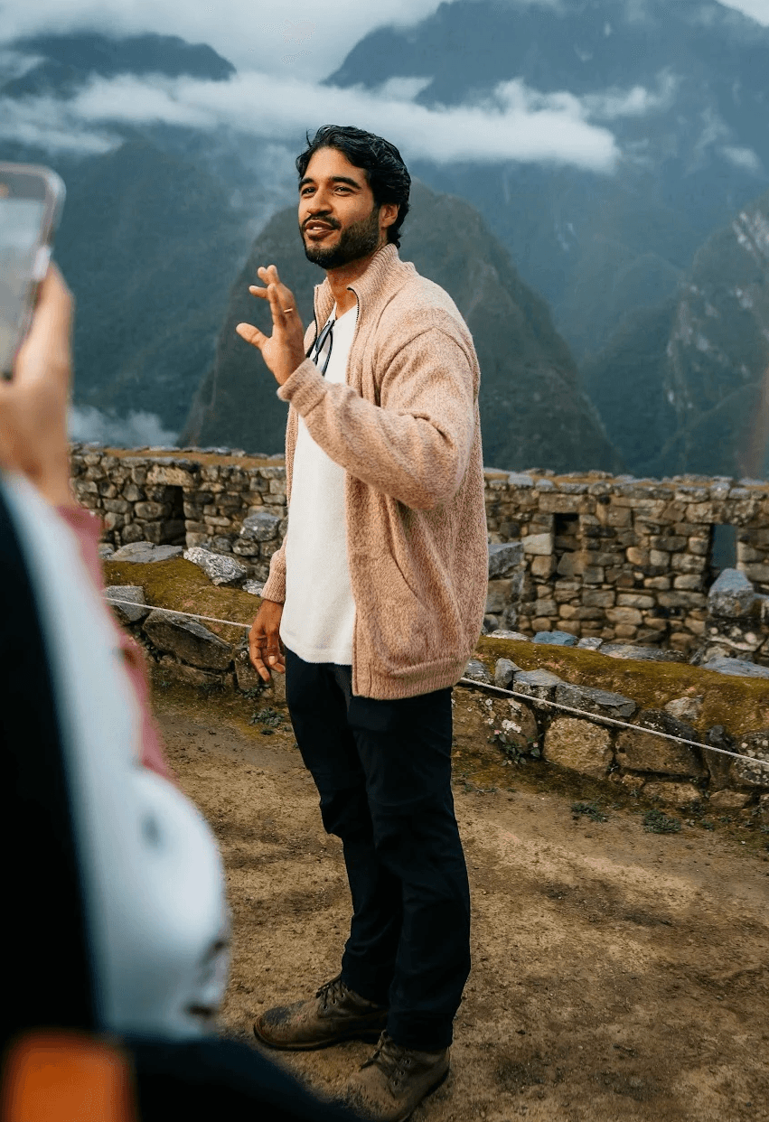 A smiling young man with crossed arms, wearing a plaid shirt and white t-shirt, poses against a dark background.