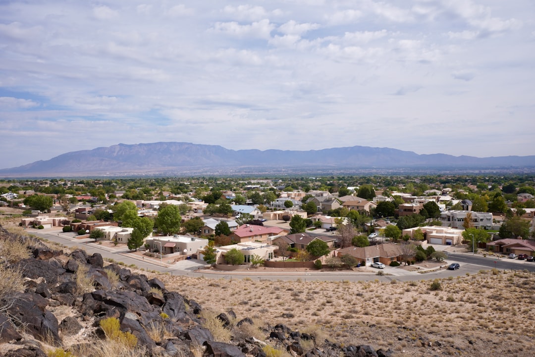 Residential neighborhood viewed from a rocky hillside with mountains and clouds in the background.