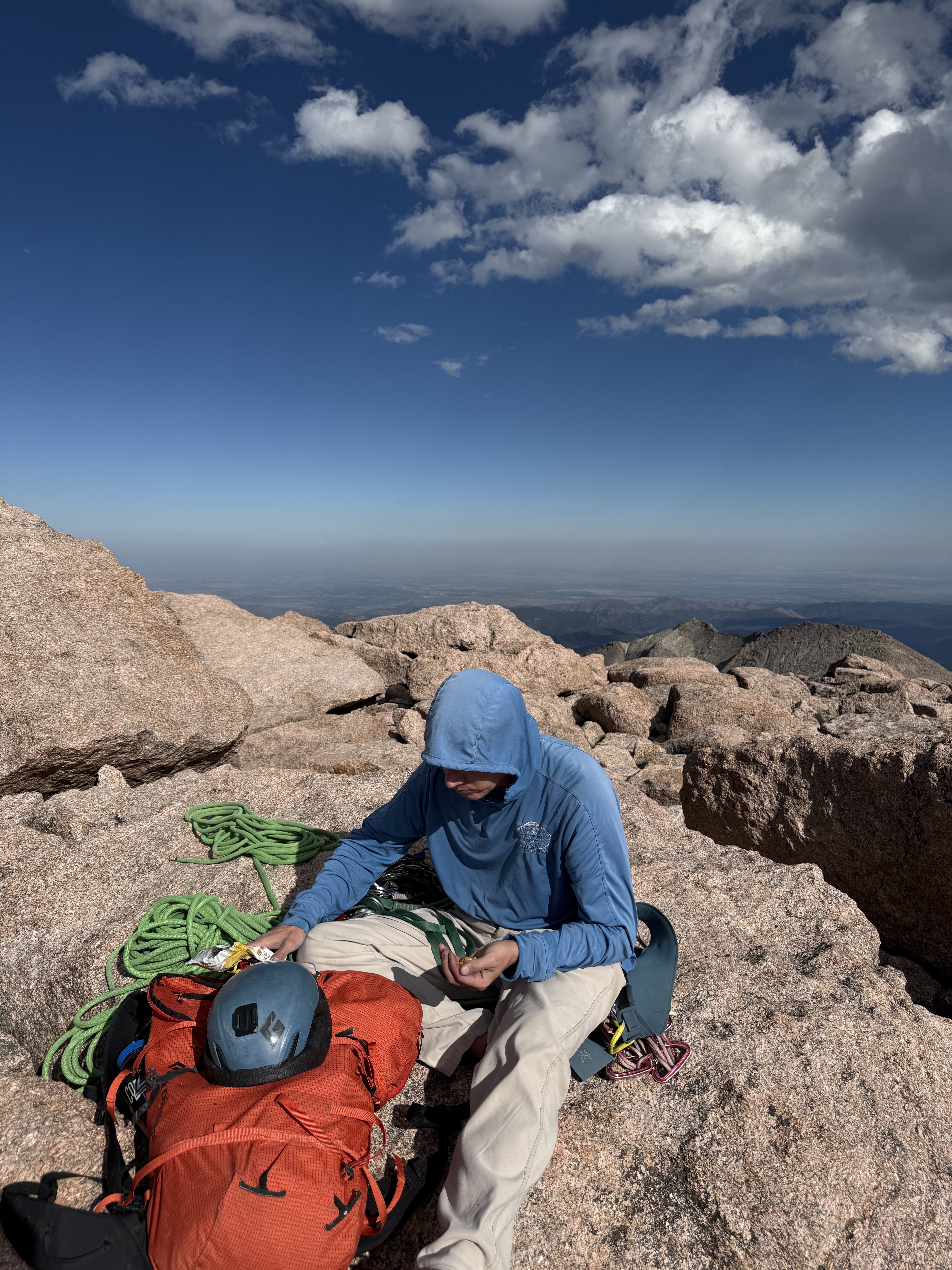 Author sitting on the summit of Long's Peak eating food and reorganizing backpack