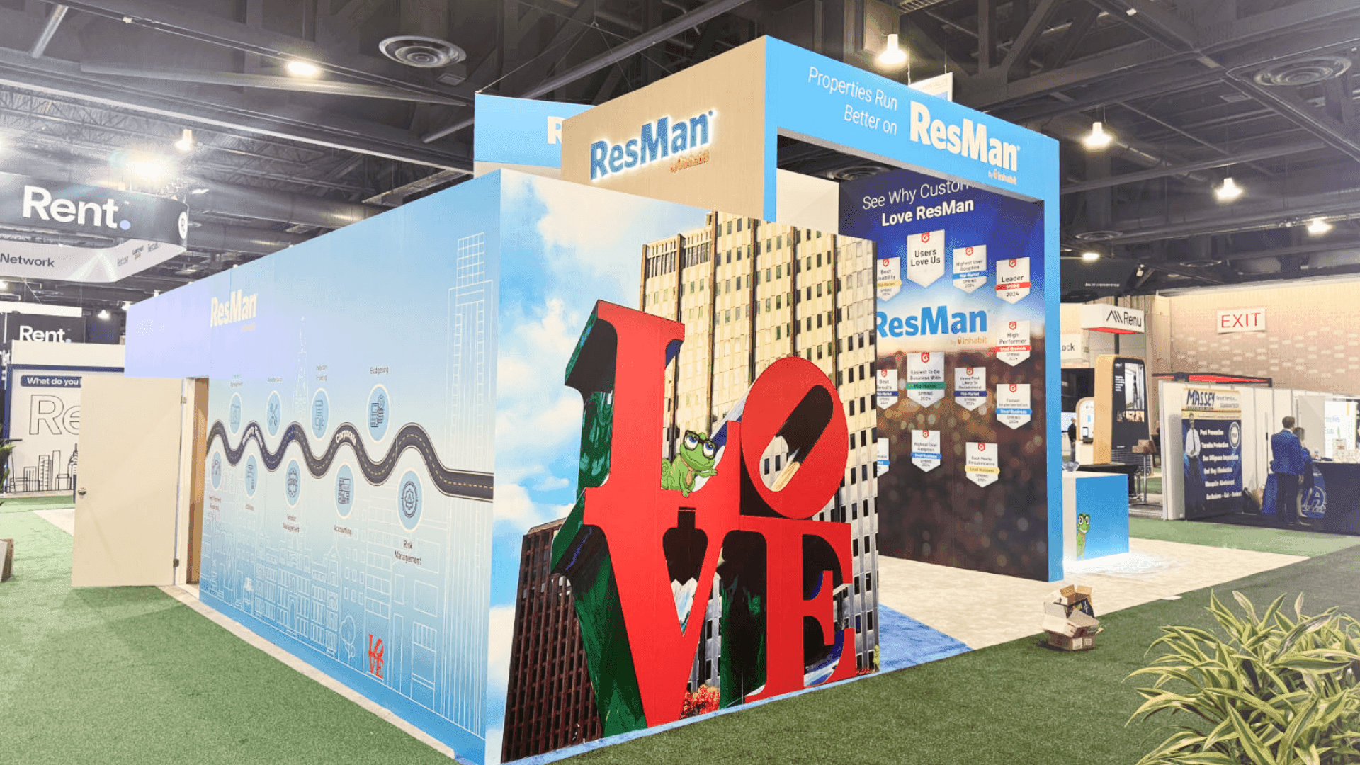 ResMan NAA 2024 large island lounge and demo booth with blue carpet, soft seating, white cube stools, software message panels, and overhead ResMan hanging signs.