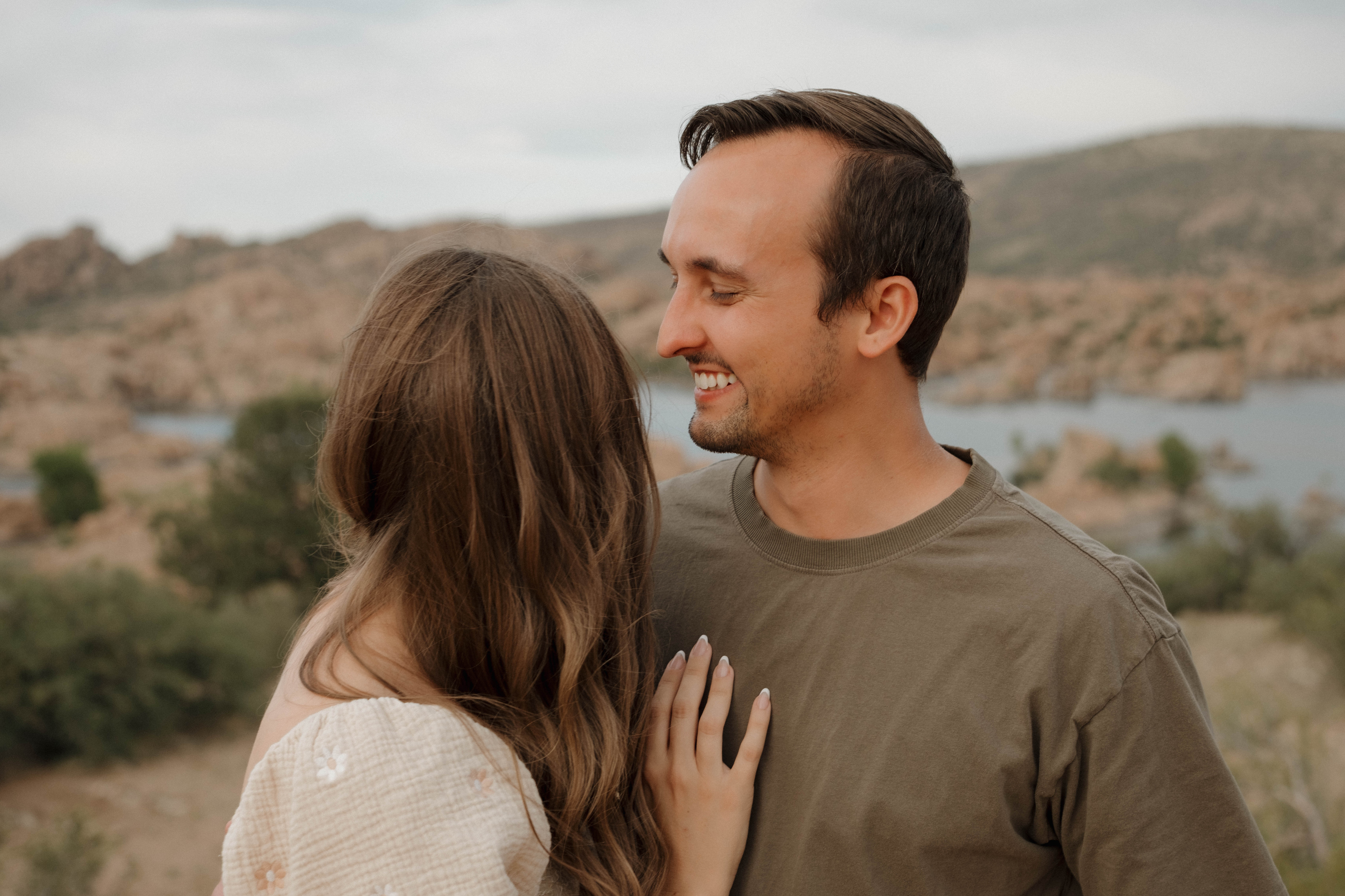Couple sitting on a blanket in the Arizona desert with two small dogs, looking at each other during a sunset couples photoshoot in San Tan, Arizona.