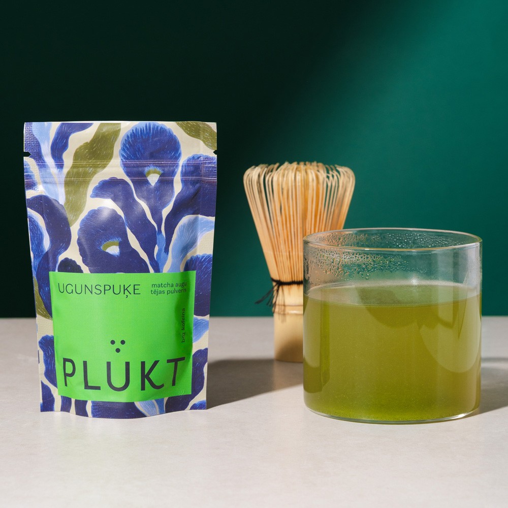 PLŪKT Ugunspuķe tējas iepakojuma un glāzes kompozīcija ar zaļu fonu — dabīgo tēju un dzērienu produktu fotogrāfēšana Rīgā.
