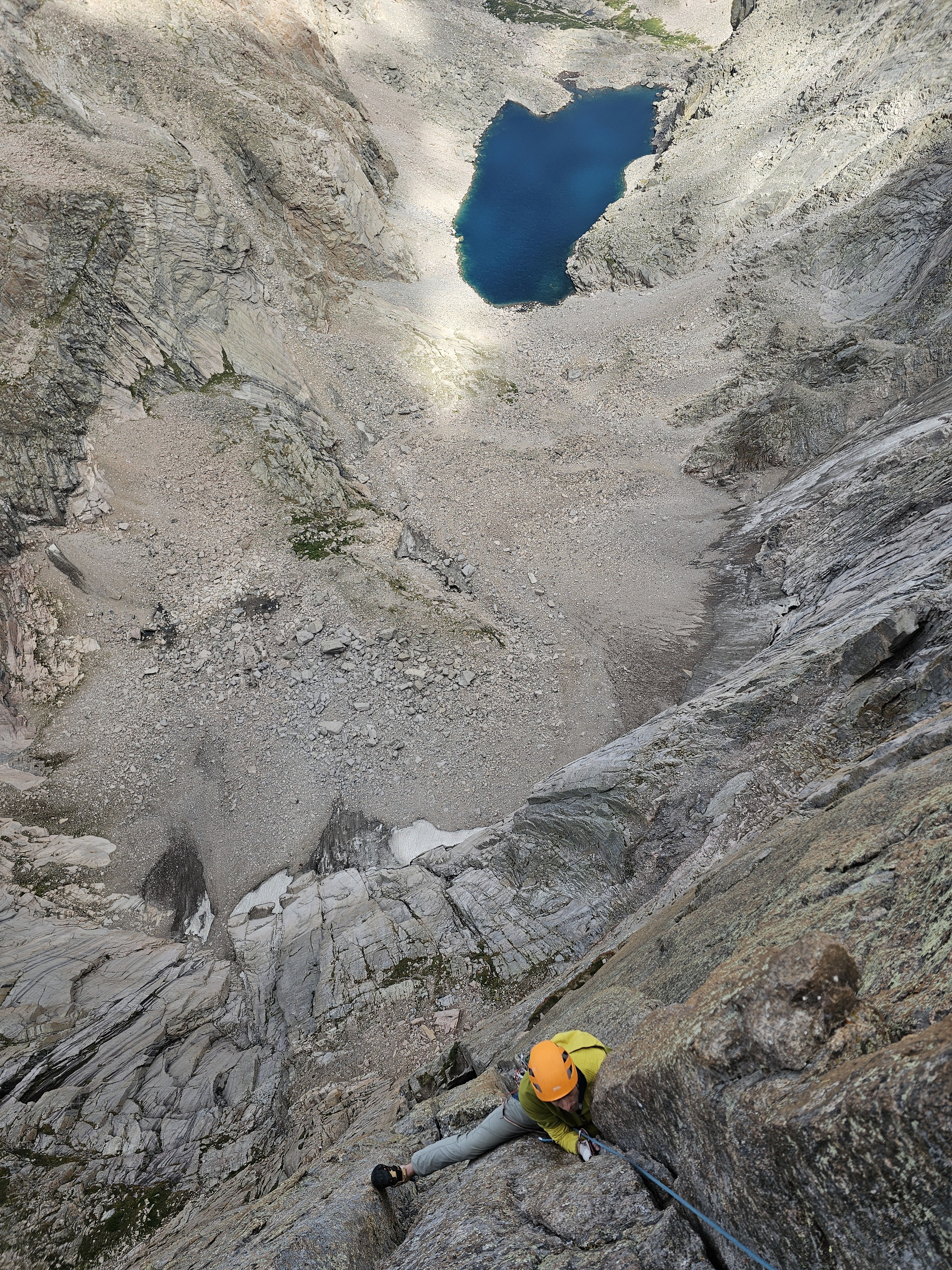 Climber jams in the crack above the crux chimney with Chasm lake in the background