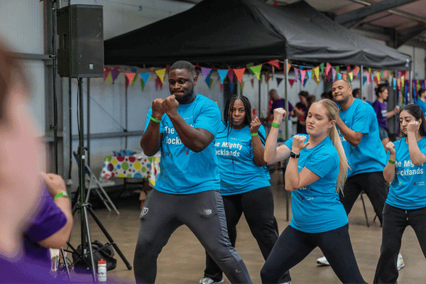 Outdoor team-building event with participants wearing matching blue shirts, taking part in inflatable obstacle courses and games, smiling and cheering, with the words 'ENTER A TEAM' in large bold white and green text across the image.