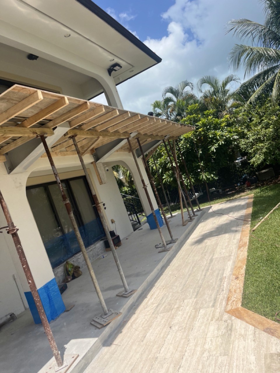 A modern hallway features vibrant teal and orange geometric and leaf patterns, with glossy tiled floors, a large rectangular light fixture, and a small shelf holding a potted plant, all leading to a large, frosted window at the end.
