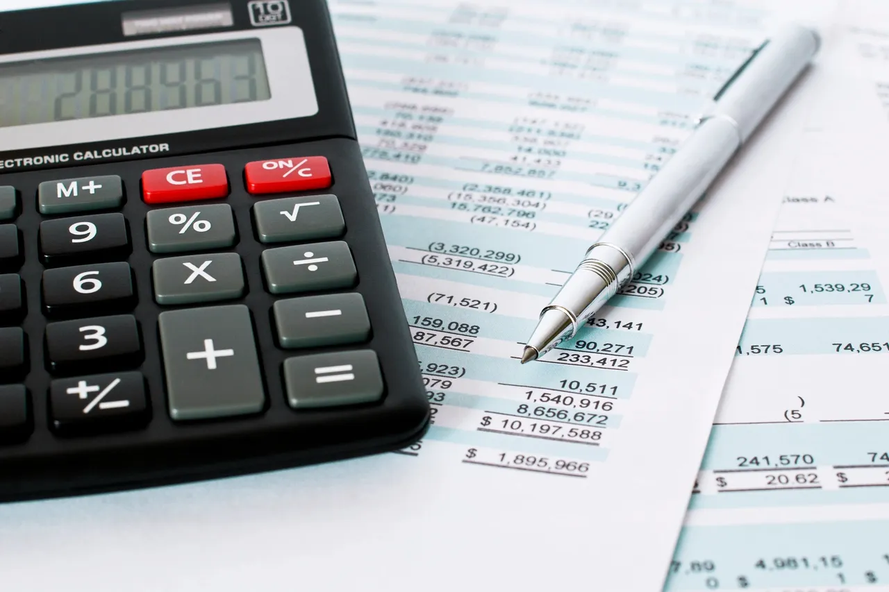 A close-up of a black electronic calculator and a silver ballpoint pen resting on financial accounting spreadsheets.