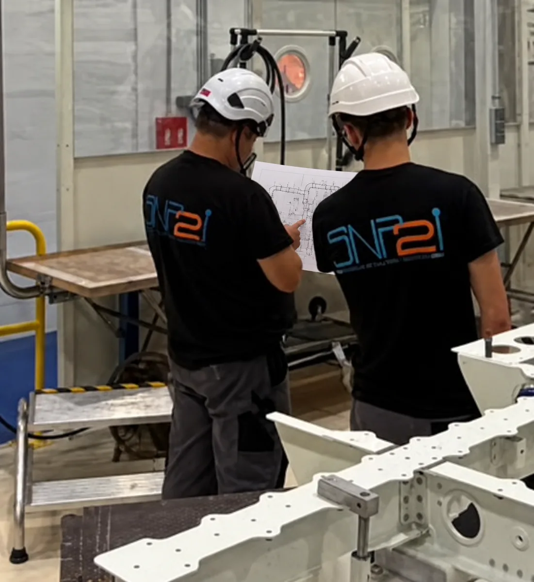 Deux collaborateurs SNP2I casqués consultent un plan sur site pour préparer l’implantation d’une solution industrielle sur mesure.