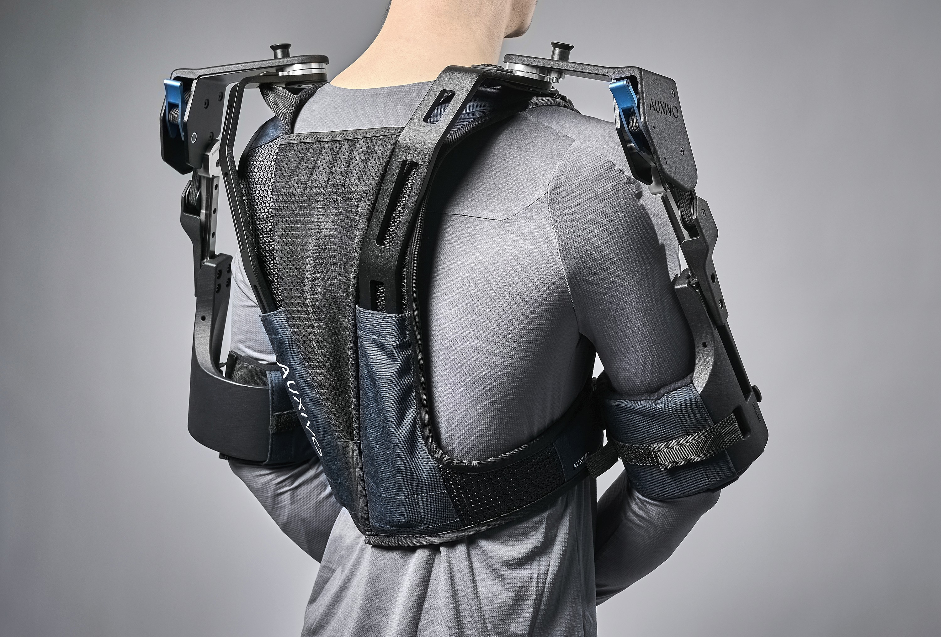 Rear view of the Auxivo DeltaSuit shoulder exoskeleton worn by a user, showing the ergonomic back structure and arm support to reduce fatigue.