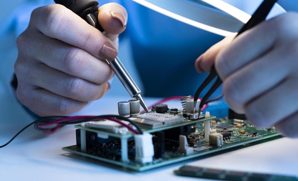 Técnico de hardware soldando placa de circuito impresso com ferro de solda, representando manutenção e reparo de equipamentos eletrônicos em TI - FindUP - Assistência técnica de informática
