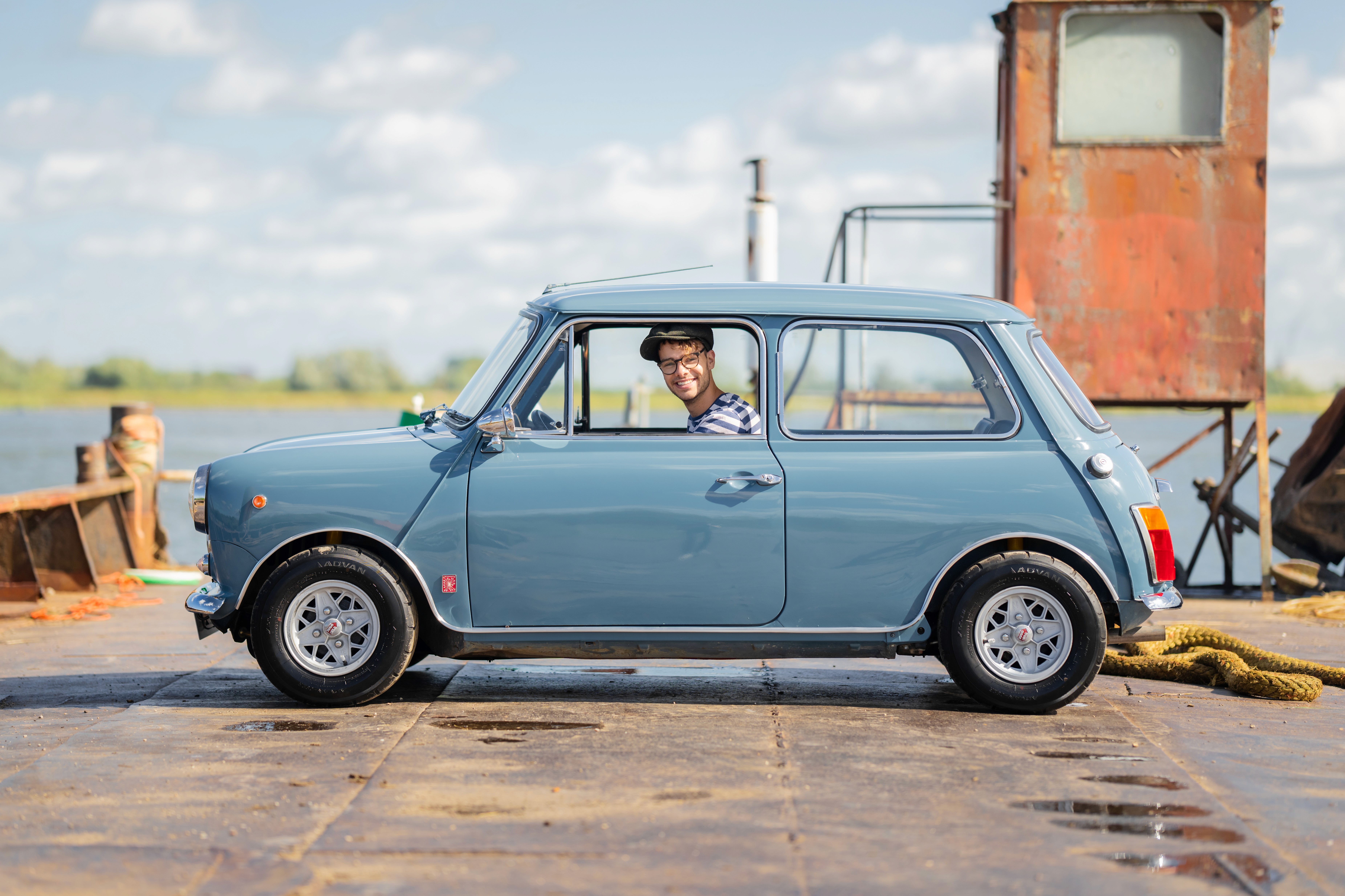 A vintage blue car parked next to a ferry, with a bright sky in the background.