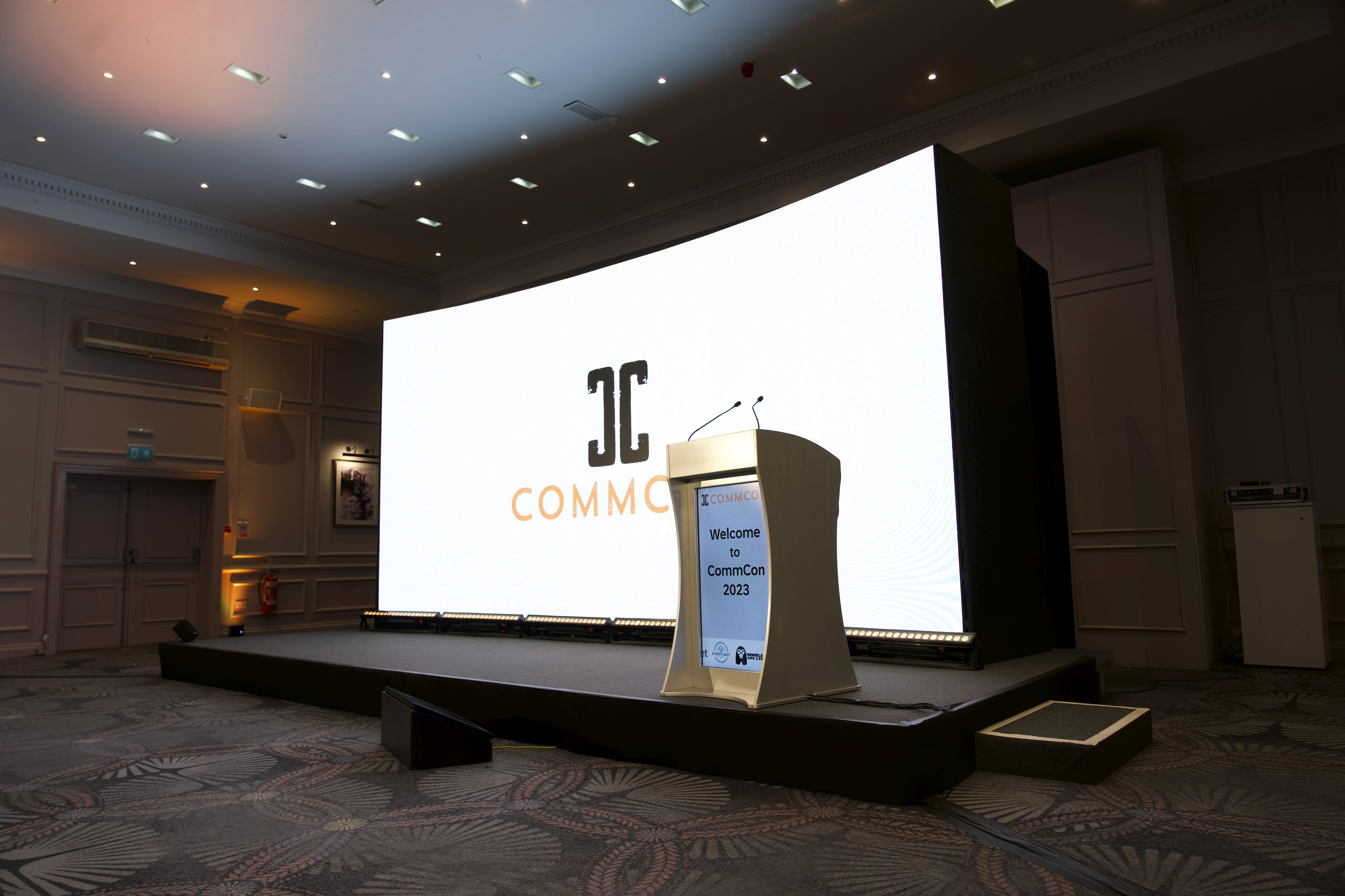 CommCon 2023 stage with a curved LED video wall, digital lectern and grey-carpeted platform