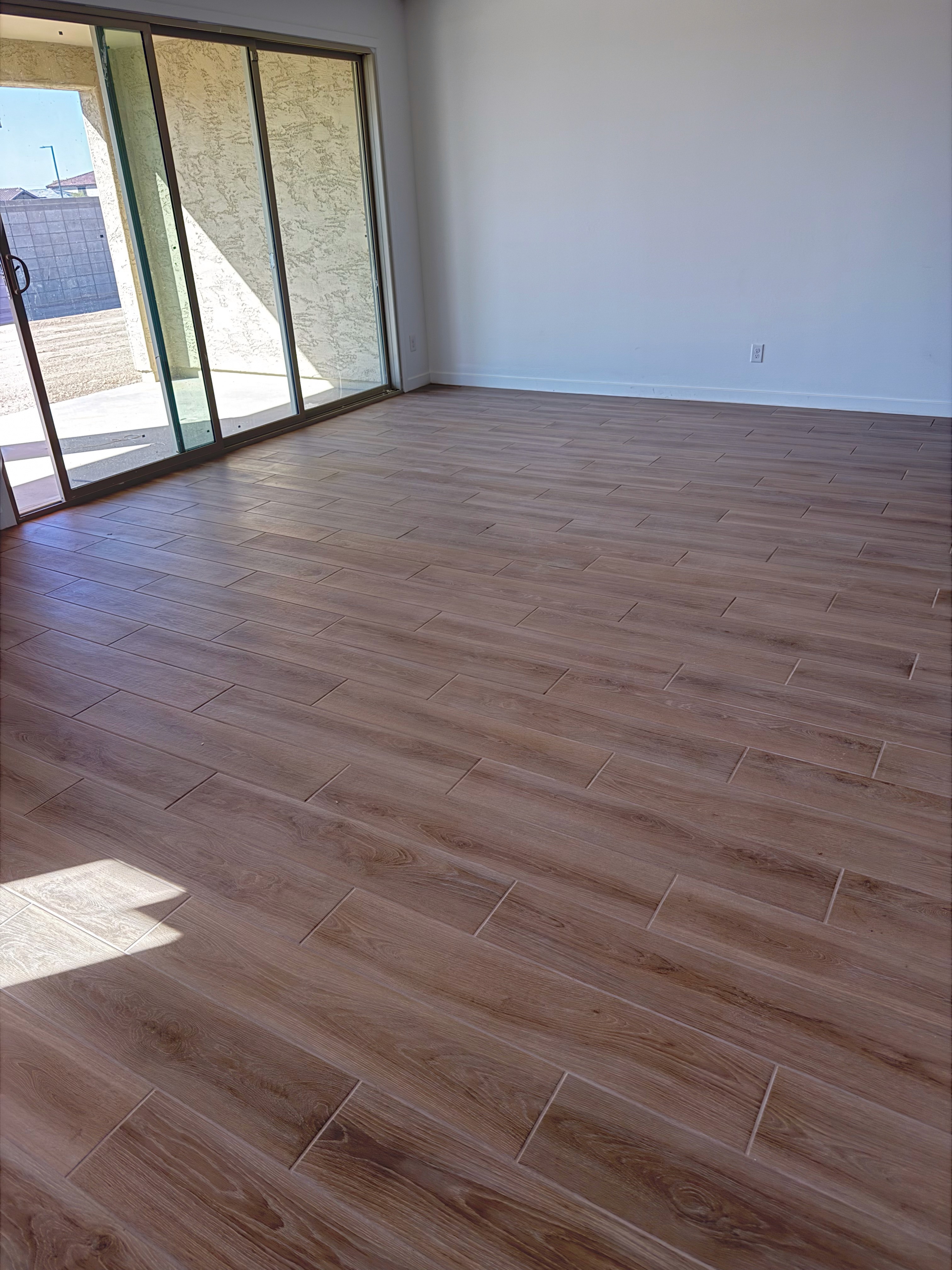 Modern living area with brown wood-look tile flooring, large sliding glass doors, and natural light in a new home under construction.