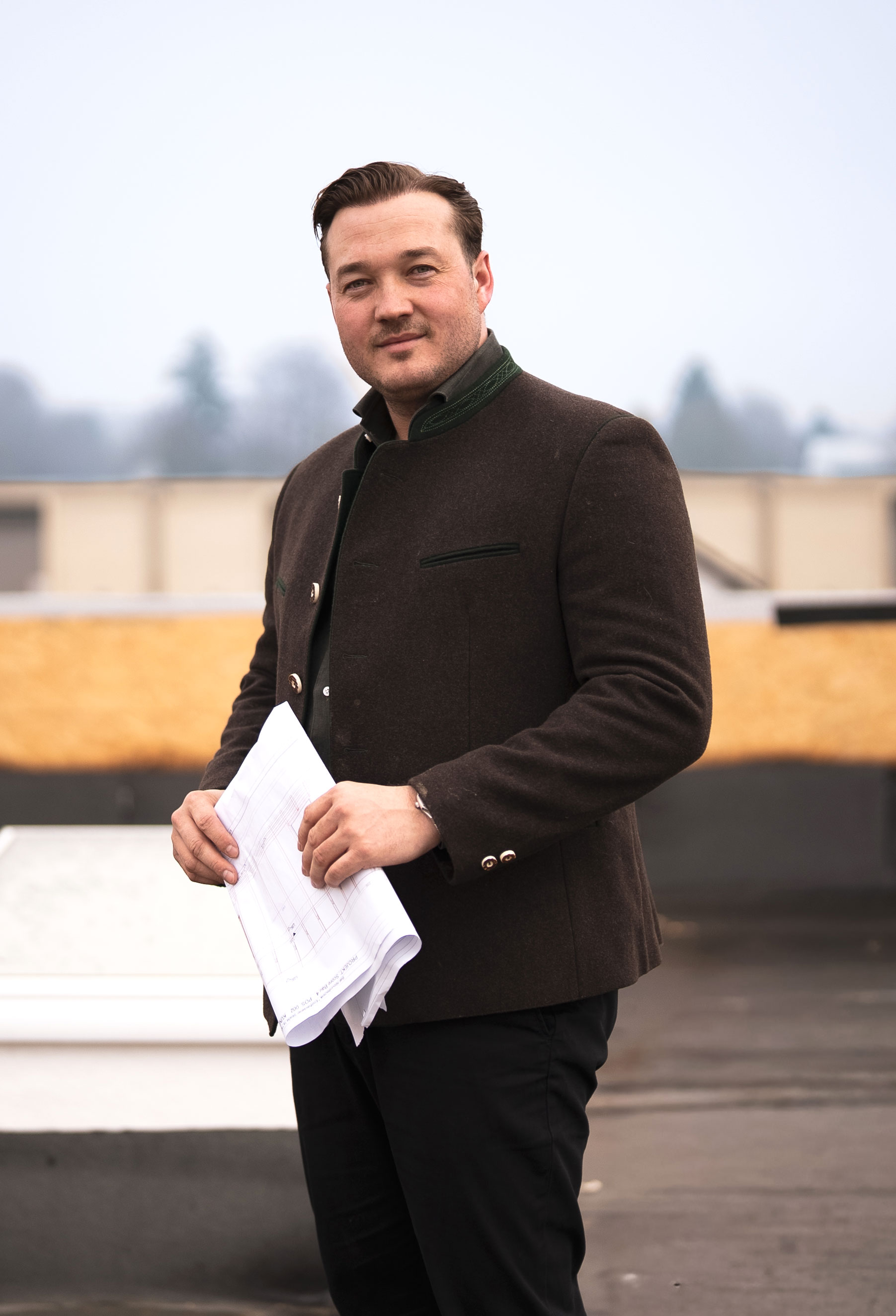 A serene outdoor seating area with two chairs, surrounded by lush greenery and a glassed-in structure.