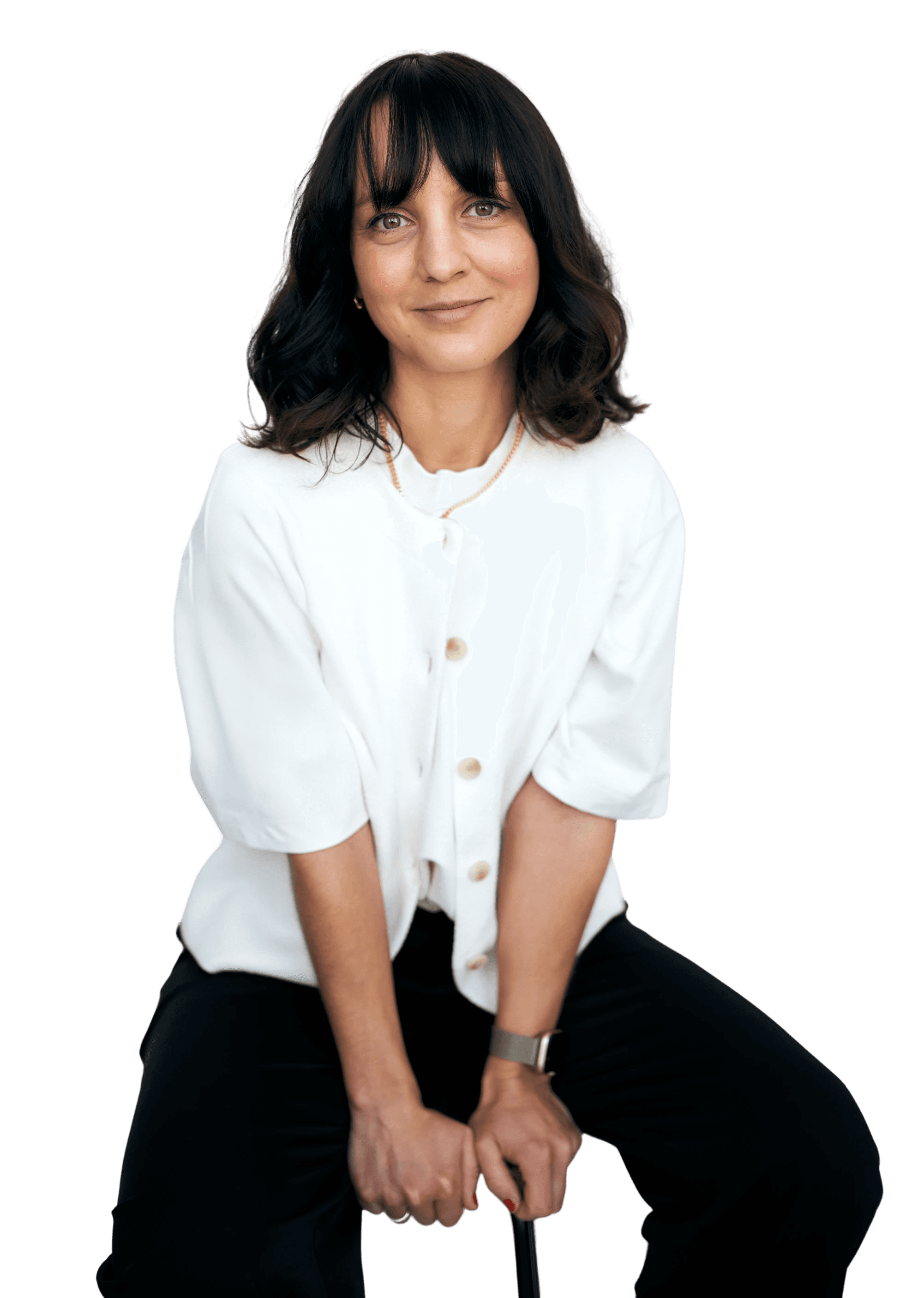 A young person with curly hair smiles at the camera while sitting in front of a laptop against a dark background.