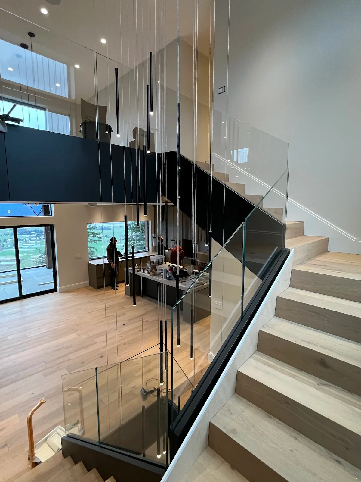 Interior staircase with sleek glass railings, wood steps, and modern pendant lighting in an open-concept home.