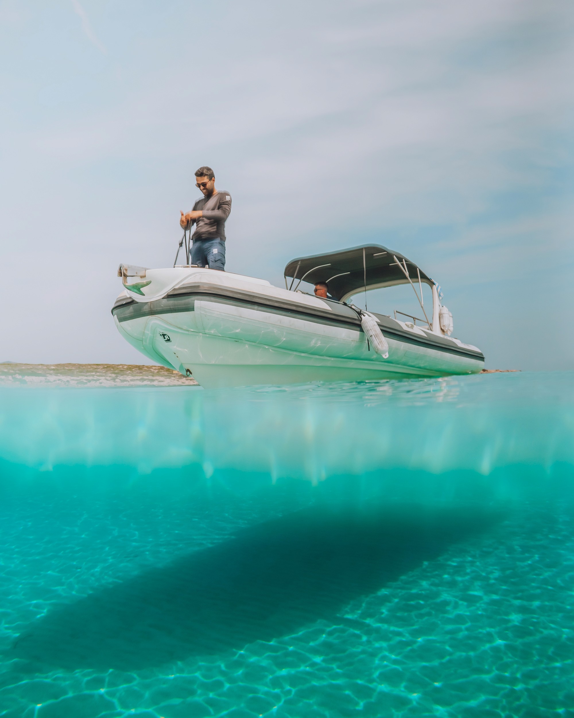 White speedboat with green hull stripe floating in crystal-clear turquoise waters with captain standing at helm under cloudy sky.