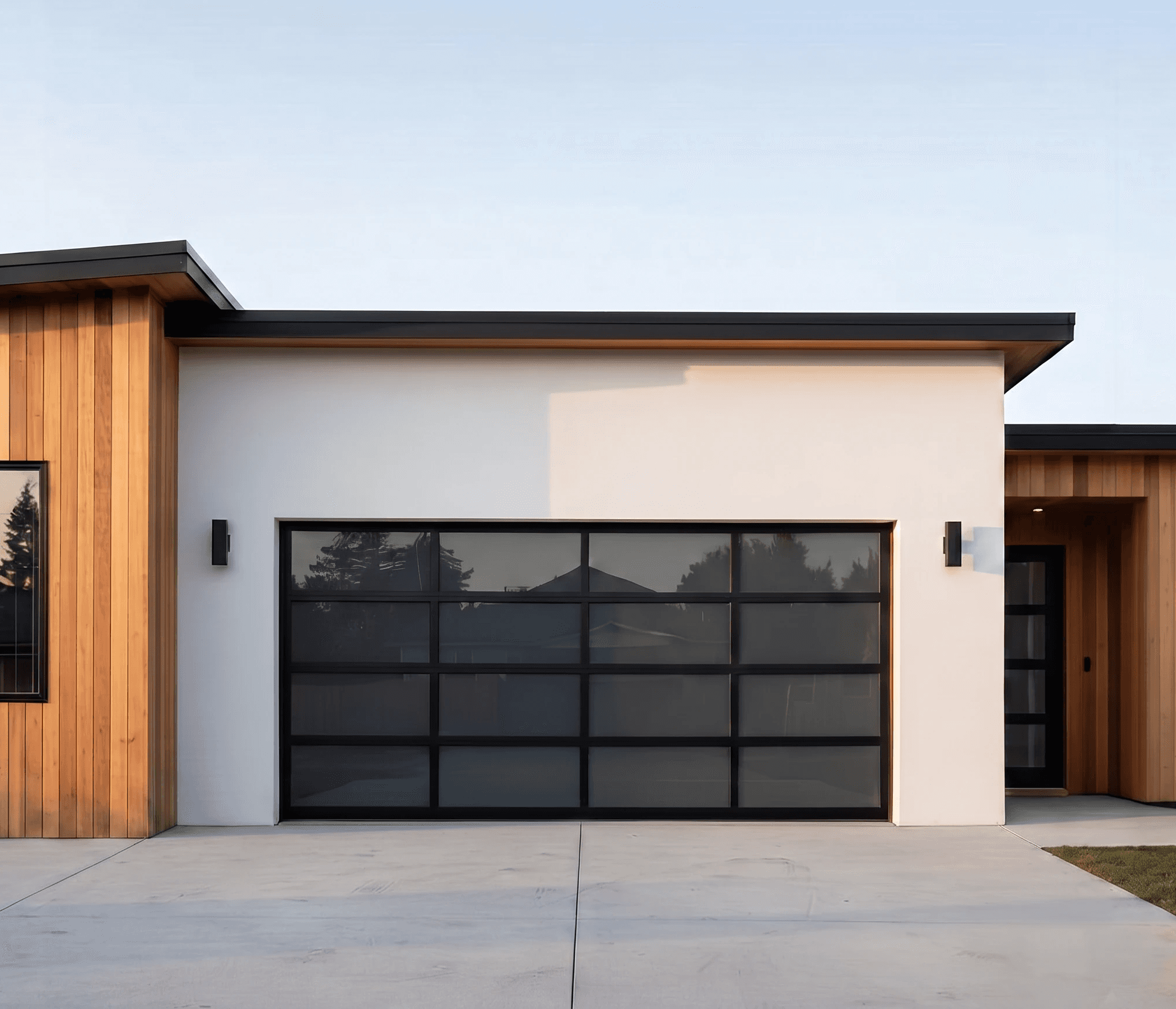 Full-view glass and aluminum garage door installed on a modern residence. This contemporary door features a black matte frame with wide frosted glass panels, showcasing a luxury architectural finish.