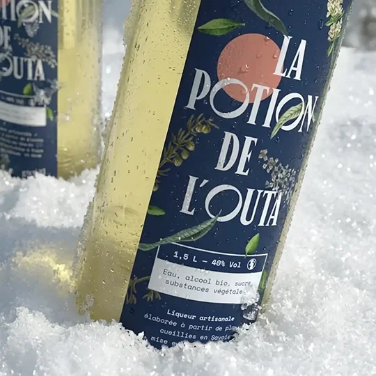 Un gros plan sur l'étiquette d'une bouteille de liqueur "La potion de l'Outa", plantée dans la neige.