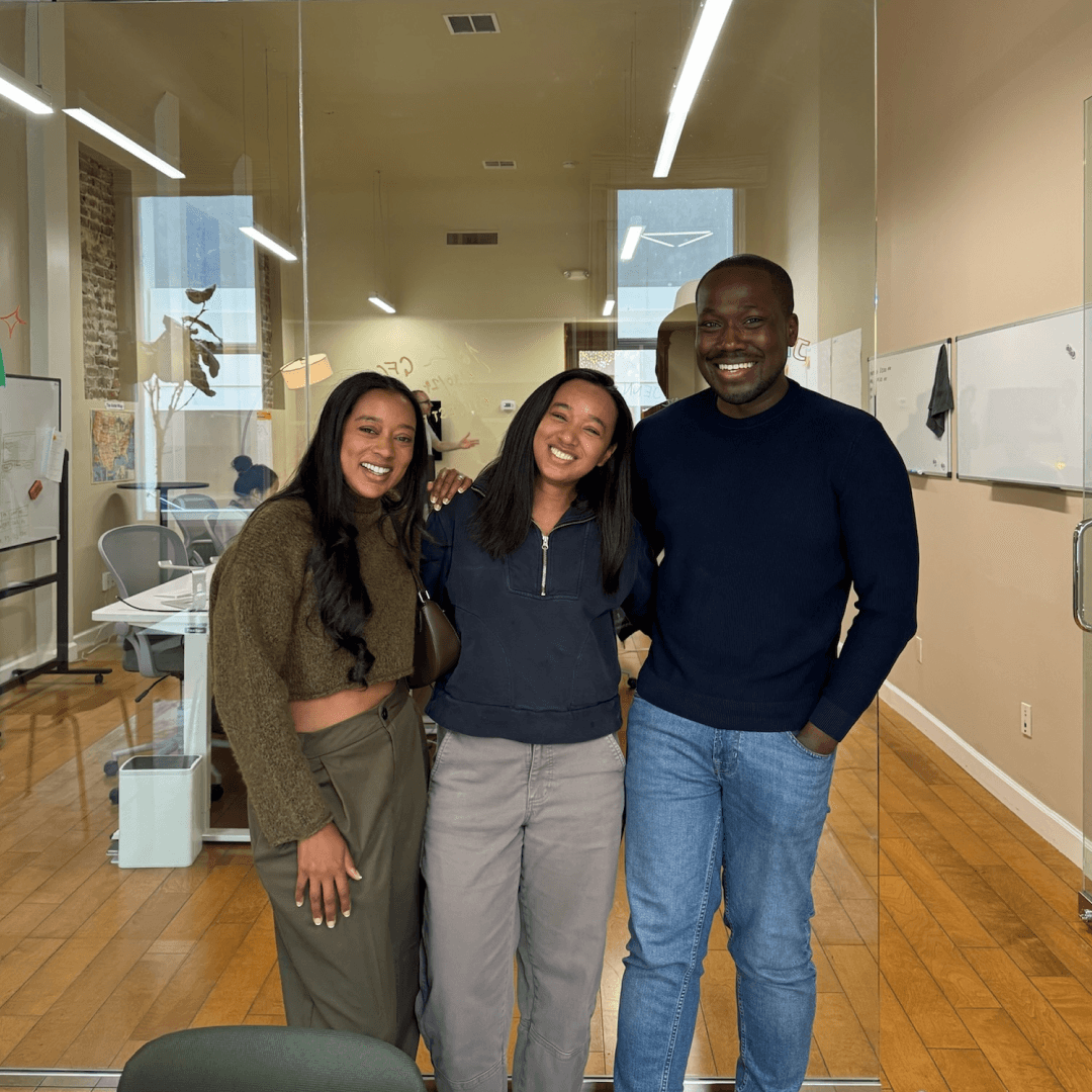 A smiling man and woman sit together on a sofa in a sunlit room, with large green potted plants in the background, embodying a warm and cheerful atmosphere.