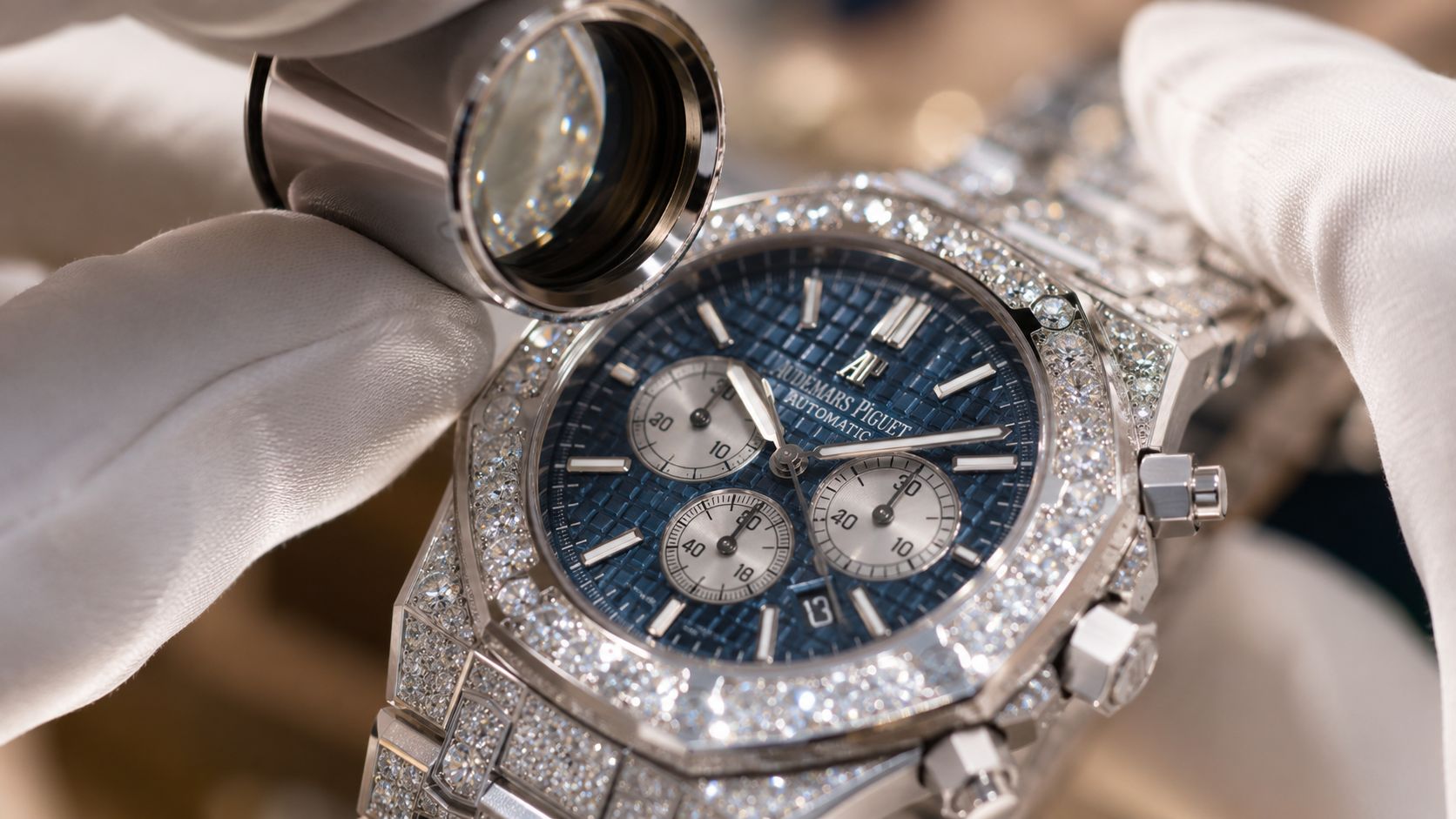 A gloved hand uses a jeweler's loupe to inspect an Audemars Piguet iced watch for men.