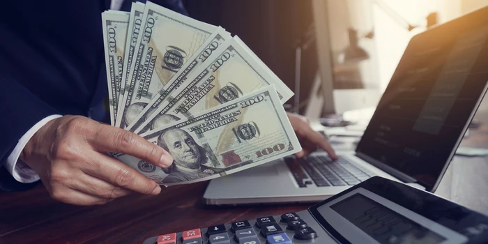 Hand handling dollars in front of datas computer | IDIGIU - Digital Marketing Agency