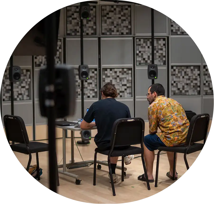 Deux personnes assises de dos devant un ordinateur dans un studio immersif équipé de multiples haut-parleurs suspendus et de panneaux acoustiques.