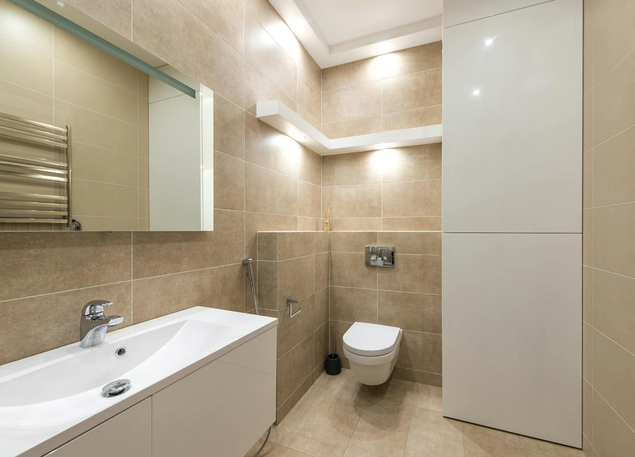 Modern bathroom in the beachfront bungalow with beige tiles, vanity, shower, and toilet.