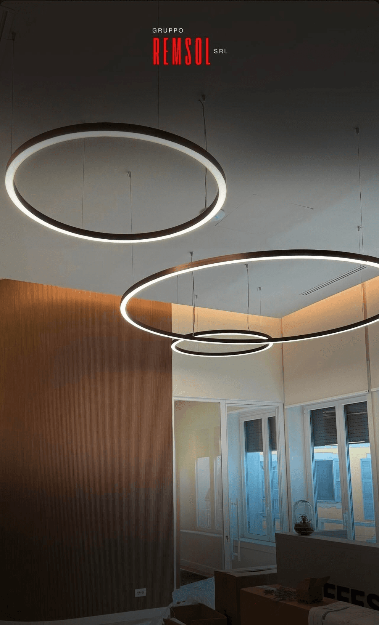 A serene outdoor seating area with two chairs, surrounded by lush greenery and a glassed-in structure.