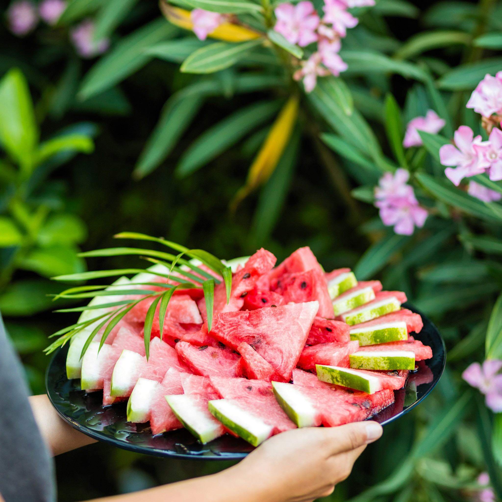 person carrying a platter of cut watermelon jungle background with florals