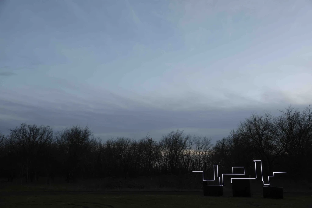 A twilight sky with soft clouds above a silhouette of trees in the foreground.