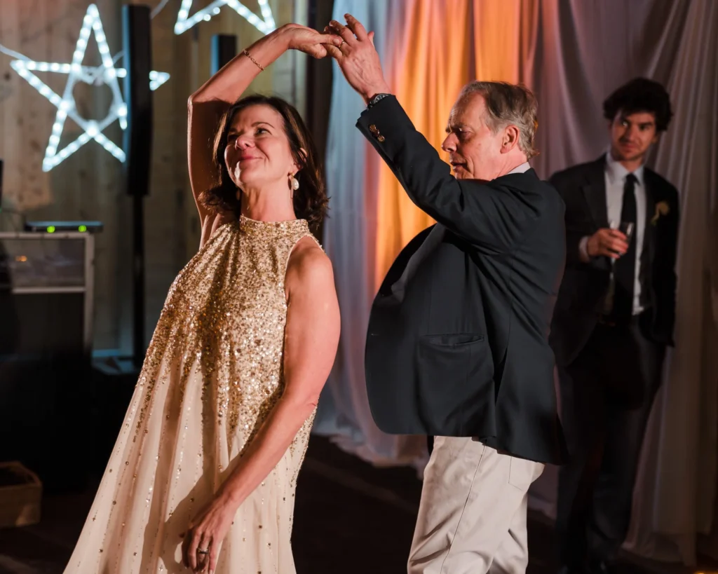 Two wedding guests dancing beneath warm reception lights
