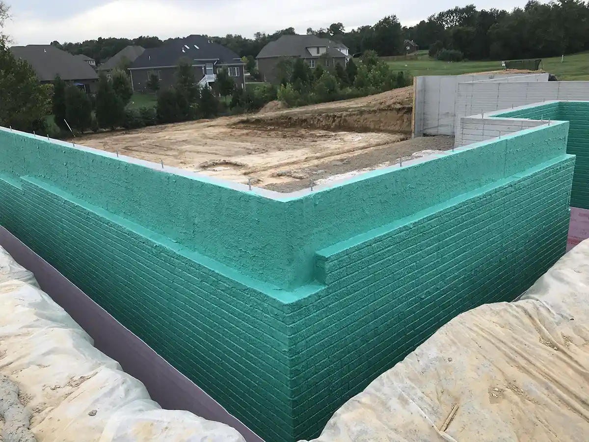 A concrete building foundation coated in teal Rub-R-Wall® (Aqua) waterproof coating