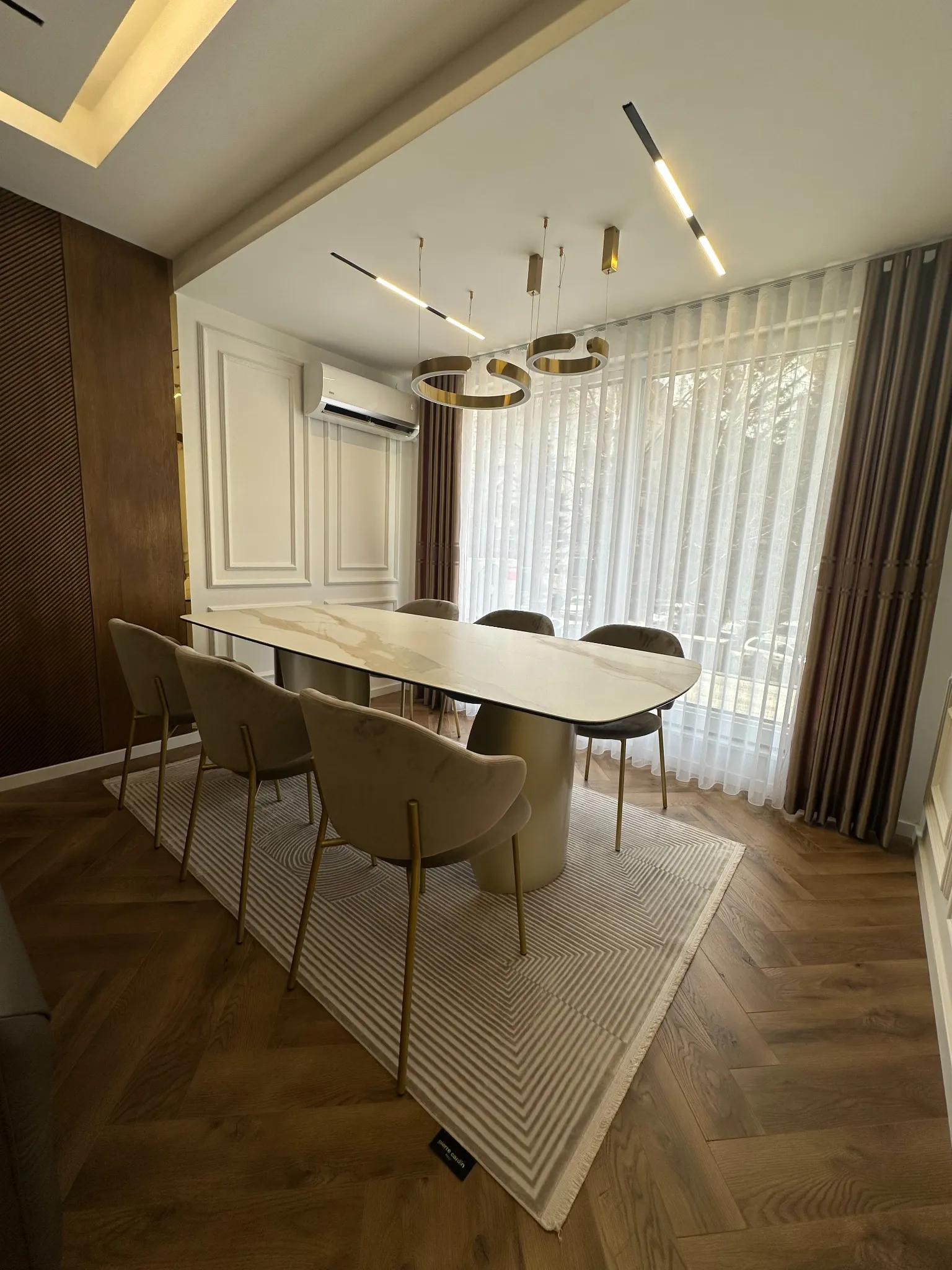 Modern dining area in a Gostivar apartment featuring custom interior design by Terraplan Partners, with a sculptural table, velvet chairs, warm wood flooring, and contemporary lighting.