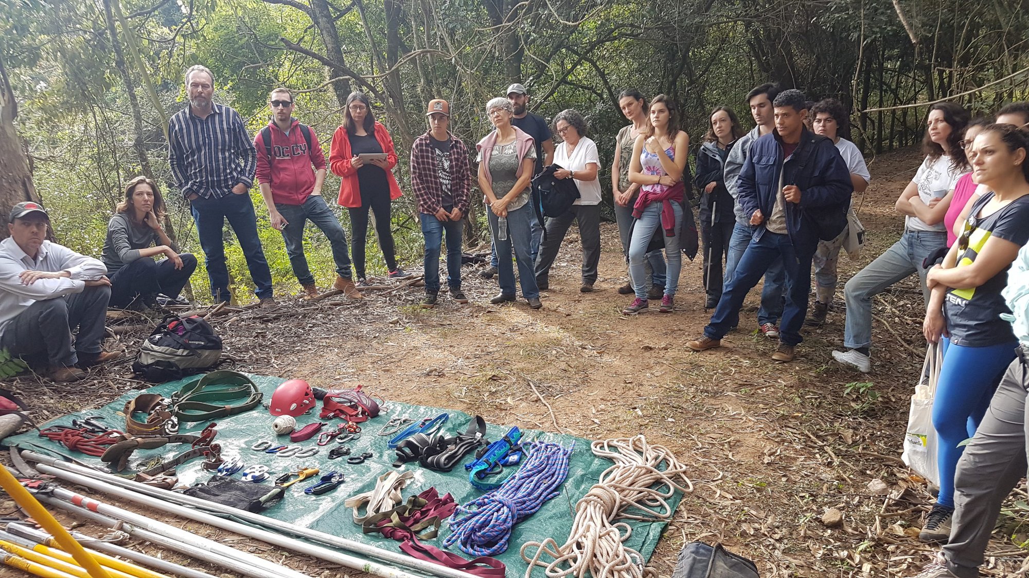 Grupo reunido em trilha na mata diante de cordas e equipamentos de coleta estendidos sobre lona