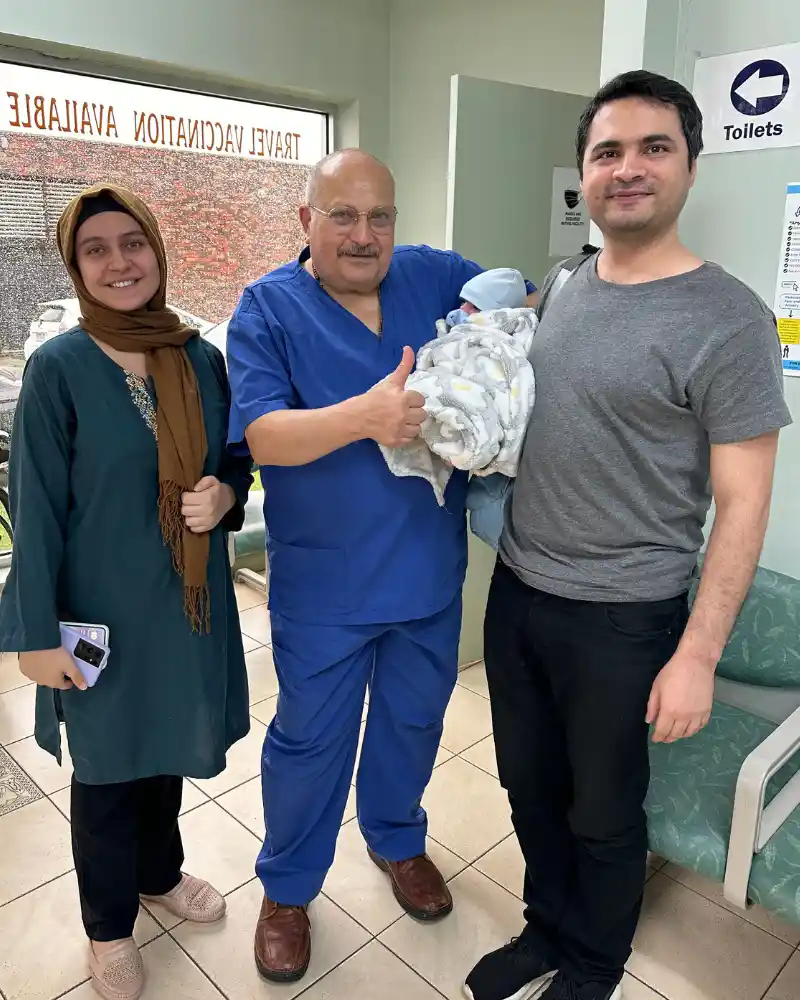 Dr. Ashraf Saddik giving a thumbs up alongside a mother and father holding their newborn baby at the Coburg clinic.