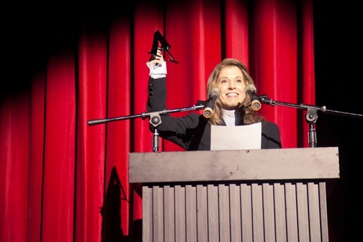 a woman on a stand with a hand raised in the air, and she has a spotlight on her