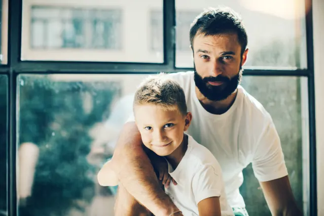 Padre con barba abrazando a su hijo pequeño en casa, imagen de la protección familiar que ofrece un seguro de vida Allianz en Murcia