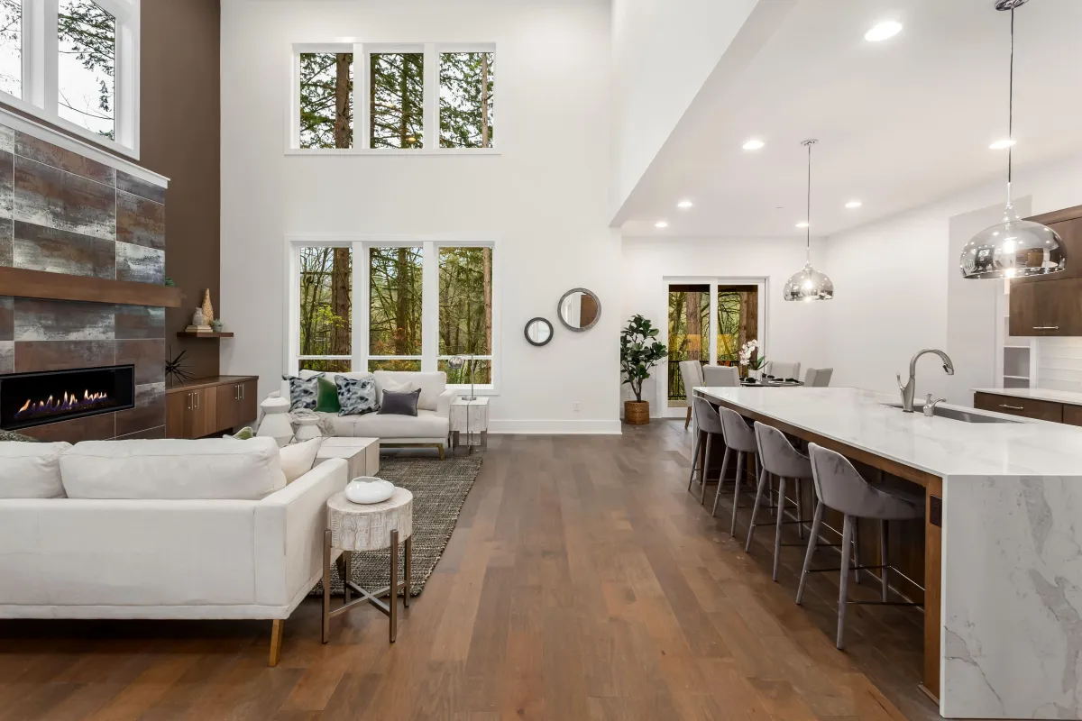 Modern open-concept living space renovated by B&Y Reno Corp, featuring white sofas, wood floors, a contemporary fireplace, and a spacious kitchen island with marble countertops.