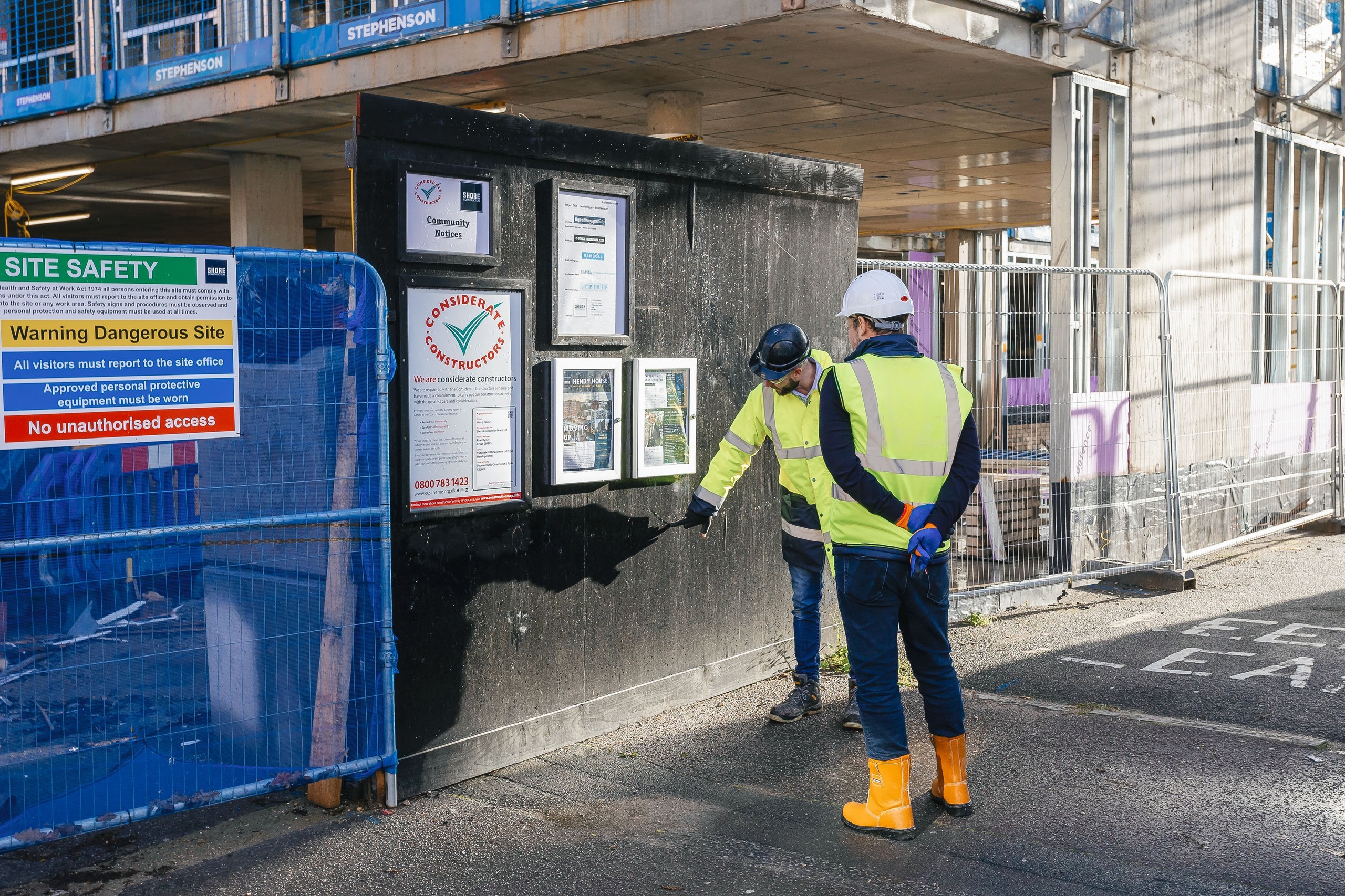 Two construction workers wearing PPE inspecting safety instructions at the gate of a construction site
