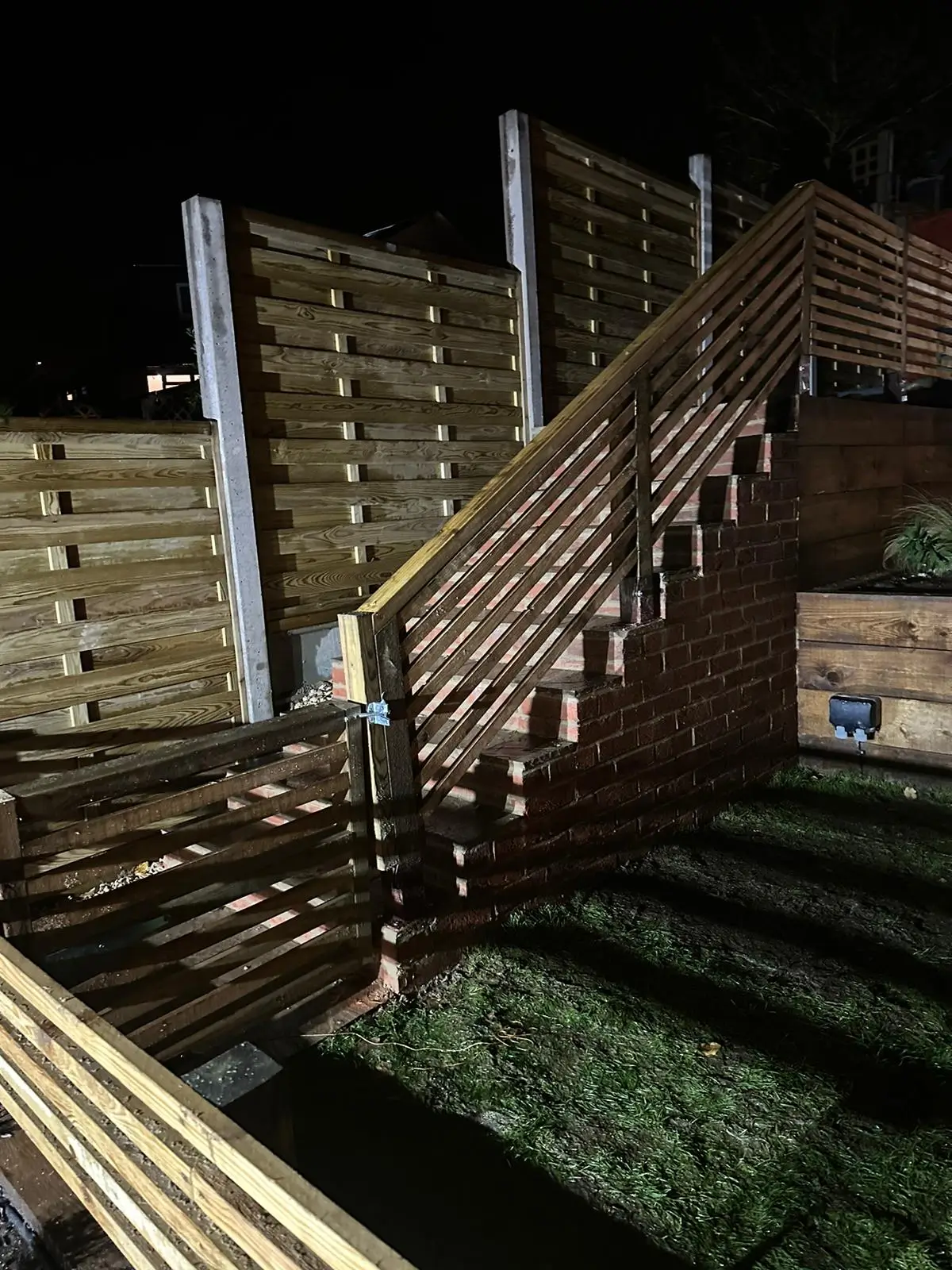 A nighttime scene featuring stairs leading up to a wooden structure, surrounded by bamboo fencing.