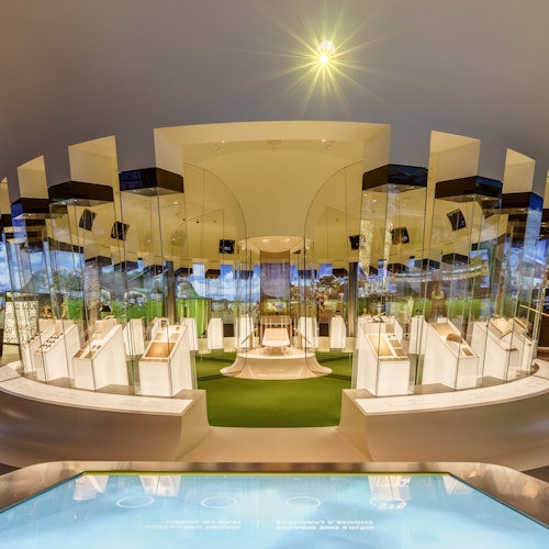 Bright, modern exhibition space featuring white display cases, reflective surfaces, and green accents under a star-like ceiling light.