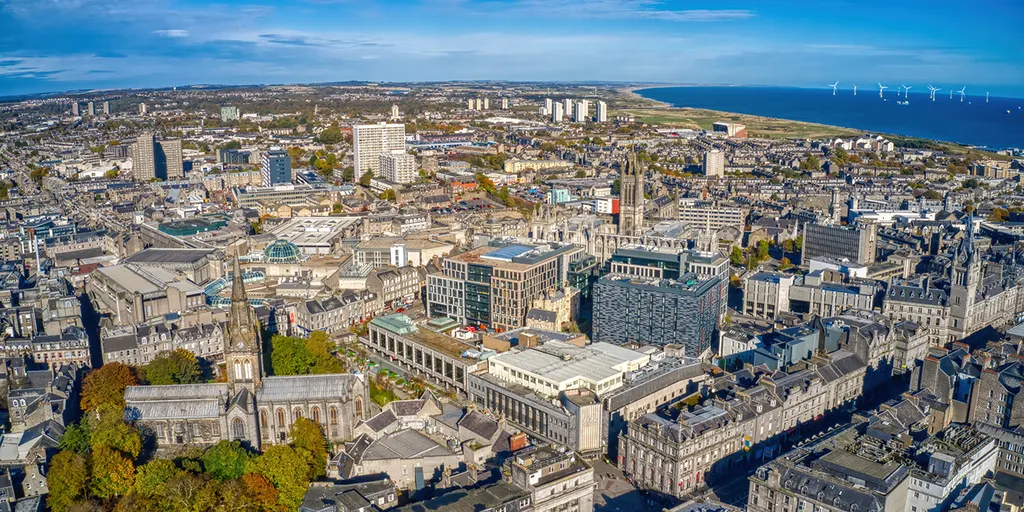 Aerial view of central Aberdeen and the coast with offshore wind turbines in the distance.