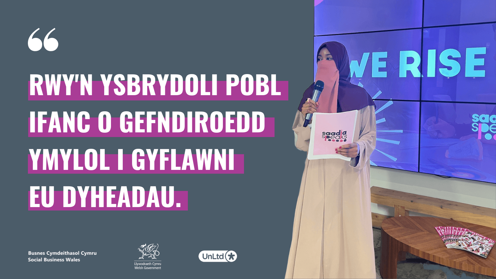 A woman in a burqa giving a talk holding a mic and a graphic of a quote in Welsh highlighted in purple.