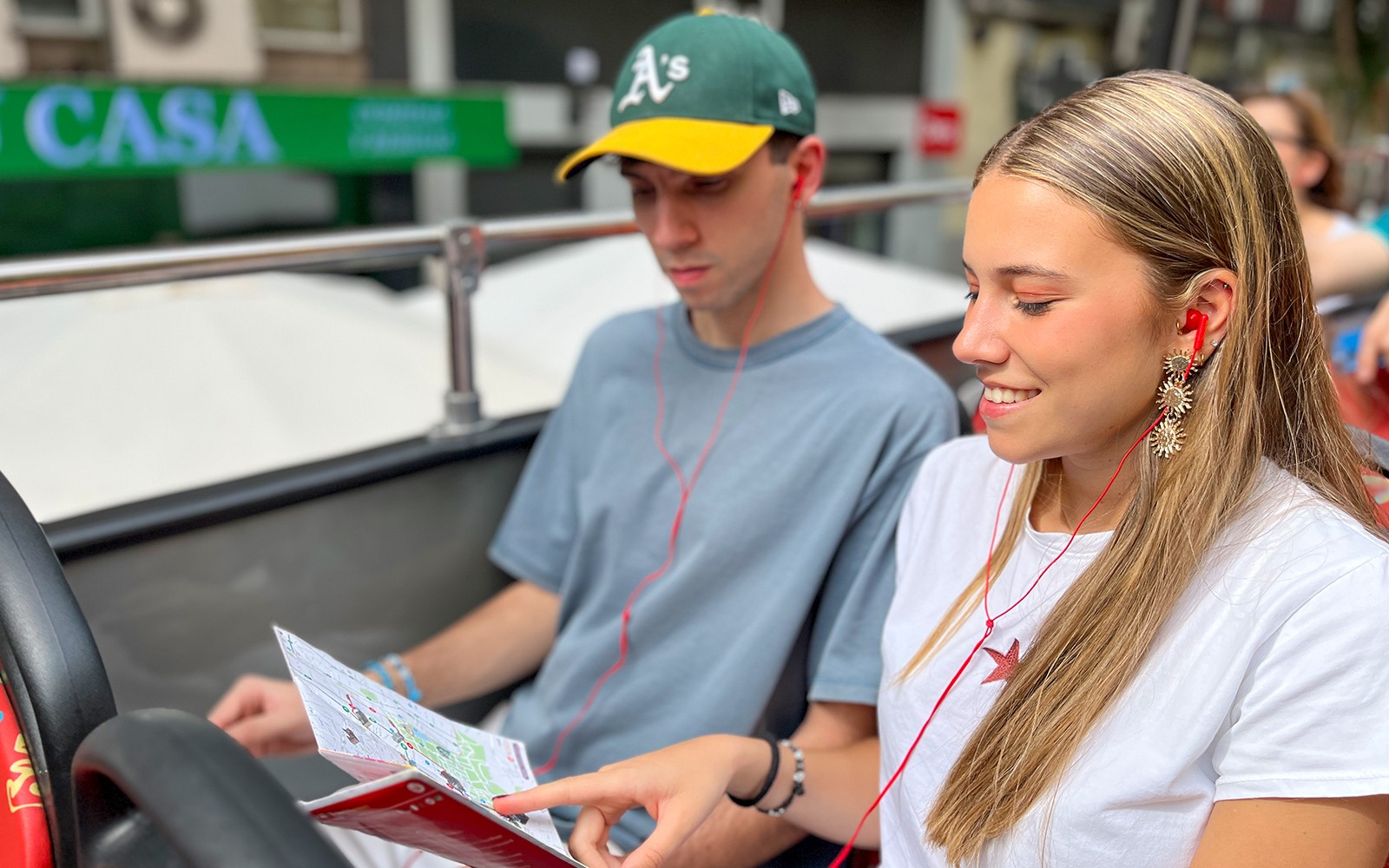 Deux touristes avec des écouteurs regardant un plan de la ville sur un bus à impériale.