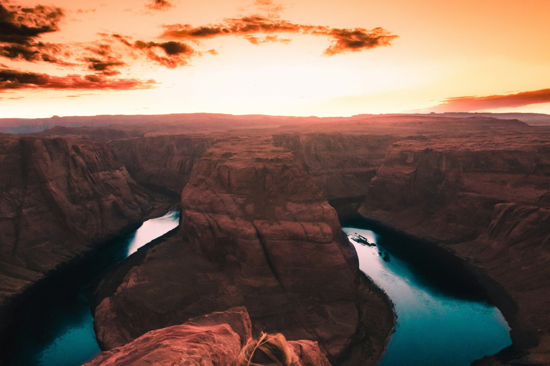 Horseshoe Bend at sunset, the Colorado River curving in a deep turquoise horseshoe around a sandstone butte under an orange sky.